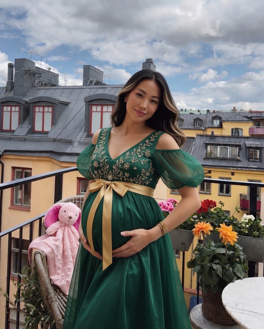 Pregnant woman in a green dress with a gold sash standing on a balcony with colorful buildings in the background.